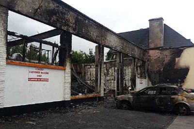 The burnt-out shell of a building, with a burnt car parked in front