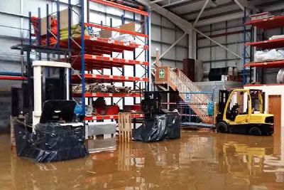 Flood water covers the floor of a warehouse with tall racking and a forklift truck