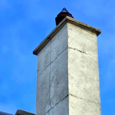 A white rendered chimney stack with cracks across its sides, against a blue sky