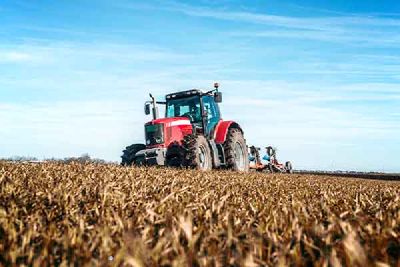 A red tractor ploughs a field of stubble