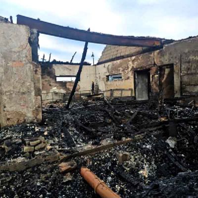 The burnt shell of a building, with charred timber and ash on the floor and a steel beam above