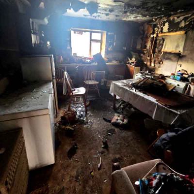A kitchen with blackened walls and ceiling, a table with a cloth, chairs and a fridge