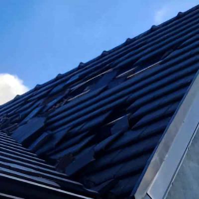 Dark roof tiles on a slope, with some tiles missing or lifted