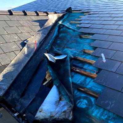 A slate roof with slates missing, showing a blue roofing membrane and timber battens