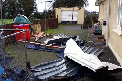 Torn sheets of metal roofing and broken timber lie in a yard beside a house